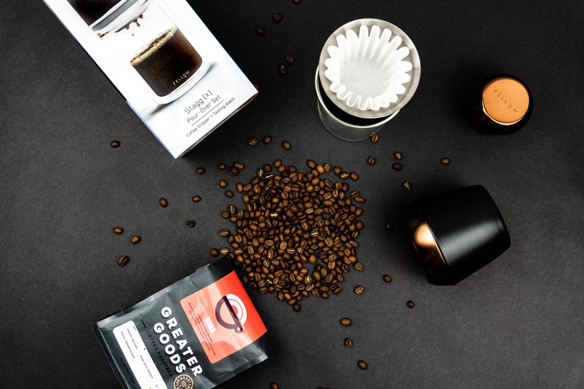 Coffee beans scattered beside the pour-over set and a bag of Greater Goods coffee