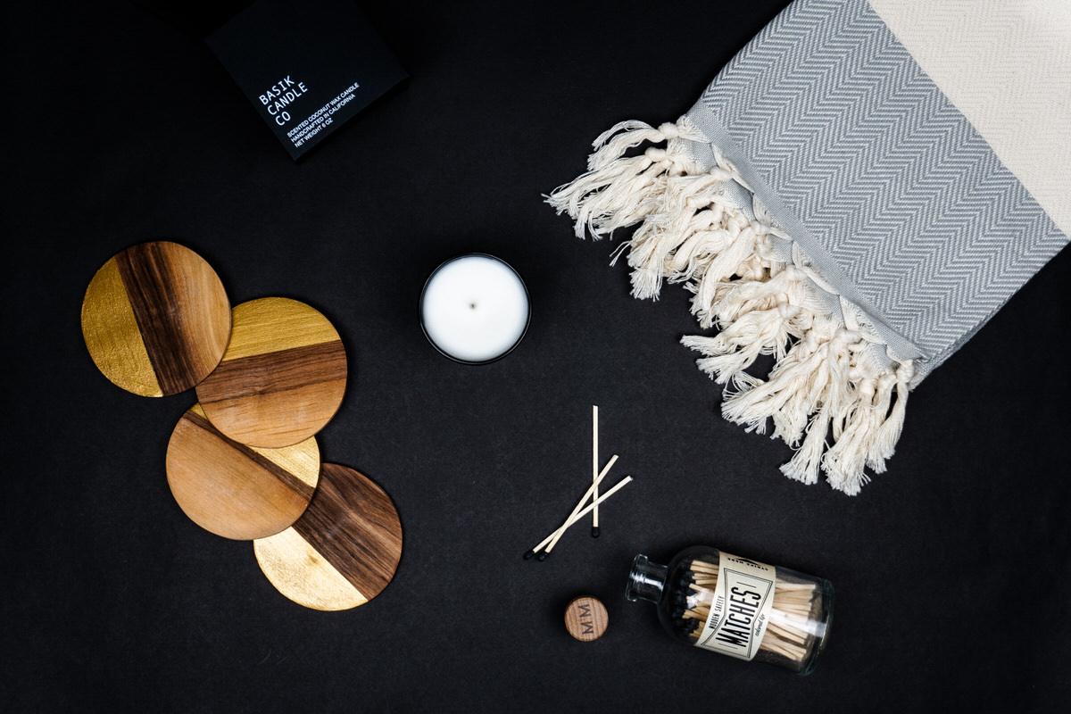 A grey Turkish towel, wooden coasters, matches, and a candle on black